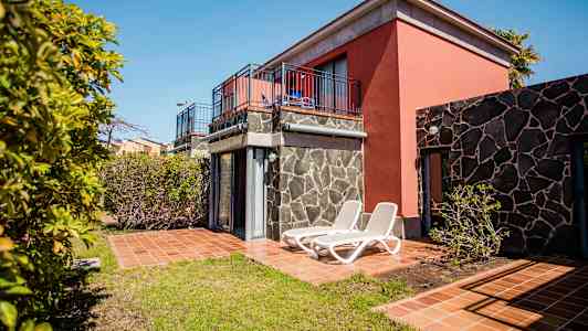 En ferieleilighet med terrasse og solsenger, omgitt av trær og grøntområder. (AI-generert tekst)