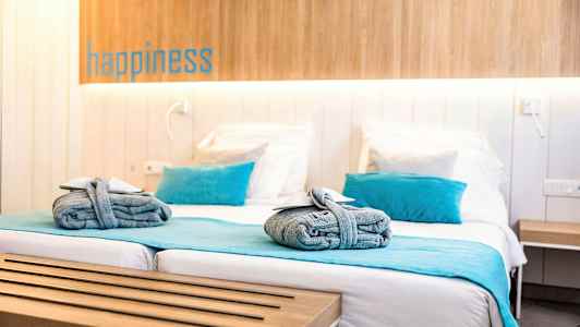 Et hotellrom med en dobbeltseng, blå detaljer som puter og sengeteppe, samt sammenrullede håndklær på sengen. (AI-generert tekst)