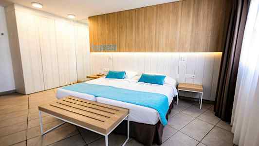 Et hotellrom med en dobbeltseng, trepanel på veggen, turkise tekstiler og bord på sidene. (AI-generert tekst)