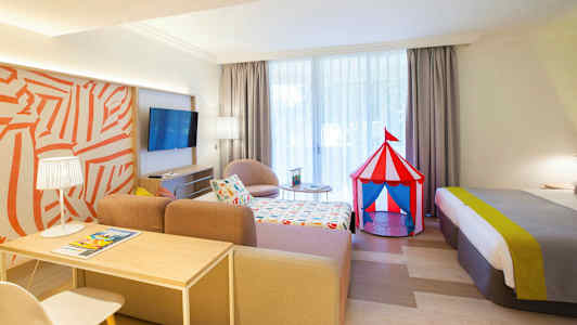 Et hotellrom med et fargerikt sirkustelt-leketøy ved siden av sengen. (AI-generert tekst)