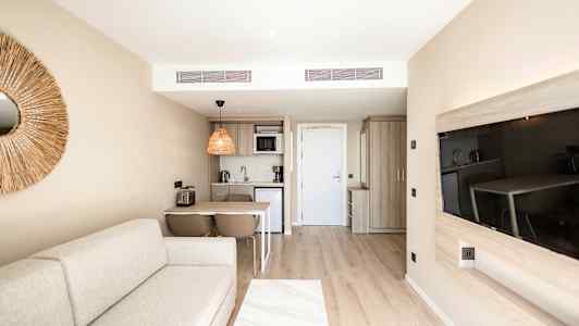 Et moderne hotellrom med komfortabel sofa, kjøkkenområde, spisebord, og flatskjerm-TV. (AI-generert tekst)