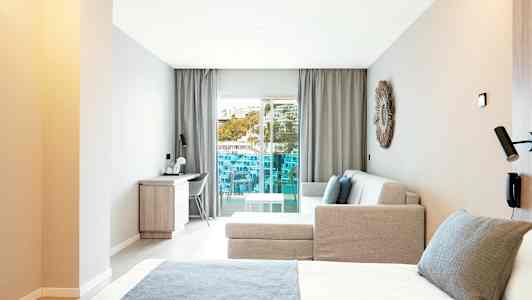 Moderne hotellrom med seng, sofa og skrivebord, samt en balkong med utsikt. (AI-generert tekst)