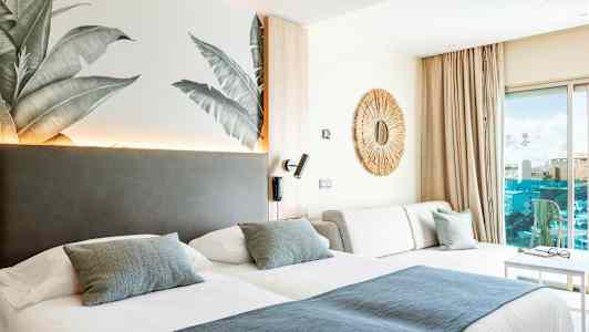 Hotellrom med to senger, en sofa og et dekorativt speil på veggen. (AI-generert tekst)