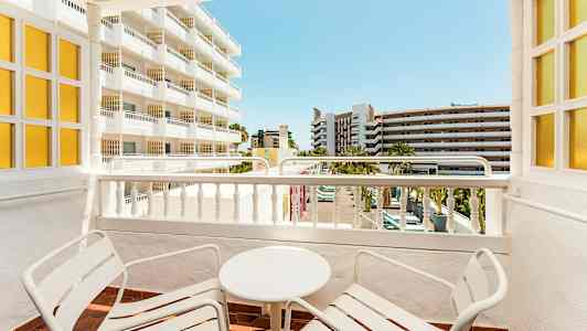 Balkong med to stoler og et bord, med utsikt over nærliggende bygninger. (AI-generert tekst)