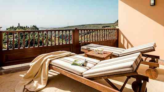 To solsenger med stripete puter står på en terrasse med utsikt over frodige åser. (AI-generert tekst)