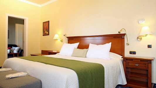 Et hotellrom med en bred seng, grønt sengeoverkast og tremøbler. (AI-generert tekst)