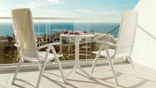 To hvite stoler og et bord på en balkong med utsikt over havet. (AI-generert tekst)