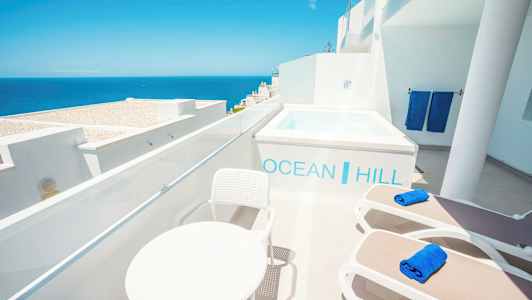 Terrasse med utsikt over havet, solsenger, bord og et lite basseng. (AI-generert tekst)