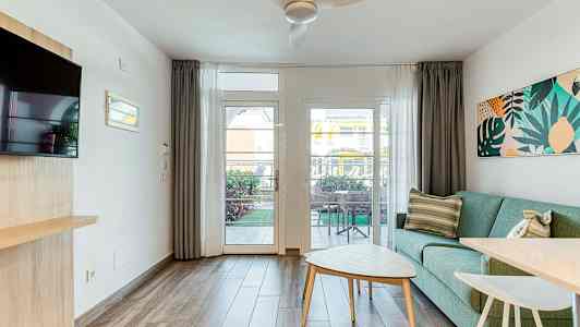 Et lyst oppholdsrom med en grønn sofa, et salongbord og utsikt mot en terrasse gjennom et glassvindu. (AI-generert tekst)