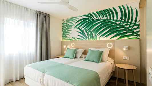 Dobbeltrom med grøn sengetøy og bladmotiv på veggen. (AI-generert tekst)