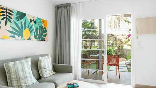 Stuemiljø med grå sofa, puter, fargerik veggkunst og glassdør som leder til uteplass. (AI-generert tekst)