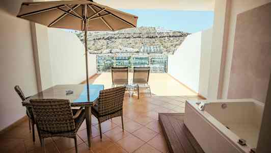 Terrasse med spisebord, parasoll, solsenger og boblebad, med utsikt over omgivelsene. (AI-generert tekst)