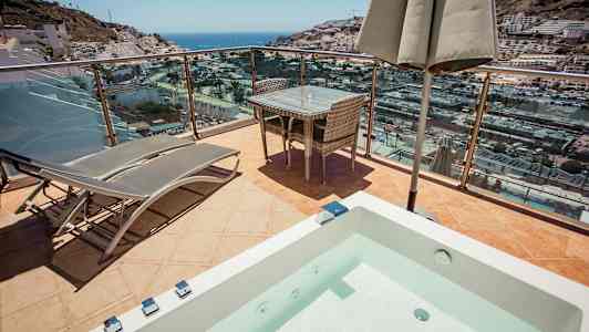 Terrasse med solsenger, bord og utsikt over havet og byen. (AI-generert tekst)