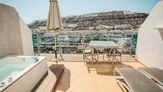 En terrasse med utemøbler, en parasoll og et boblebad med utsikt over en høyde med bygninger. (AI-generert tekst)