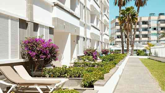 Bilde av en hvit bygning med lilla blomster og solsenger ved en gangvei. (AI-generert tekst)