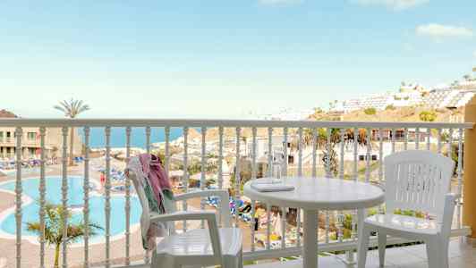 Utsikt fra en balkong med hvite møbler mot et basseng og havutsikt. (AI-generert tekst)