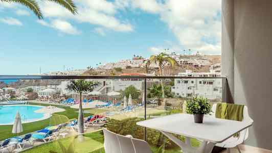 Utsikt fra en balkong med utsikt over et svømmebasseng og omkringliggende ferieanlegg på en solrik dag. (AI-generert tekst)