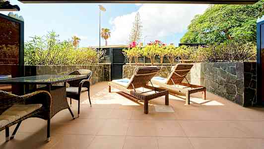 En terrasse med solsenger, bord og stoler samt omgitt av planter. (AI-generert tekst)