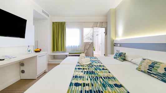 Et hotellrom med to senger, en TV på veggen, og en dør til badet. Rommet har lys innredning. (AI-generert tekst)