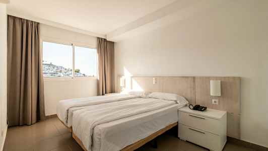 Et hotellrom med en dobbeltseng og et vindu som viser en hvit bygning. (AI-generert tekst)