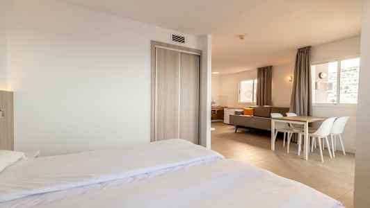 Moderne og lyst innredet hotellrom med dobbeltseng, sittegruppe og spisebord. (AI-generert tekst)