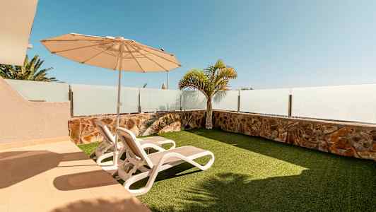 En uteplass med to solsenger, parasoll og kunstgress. (AI-generert tekst)