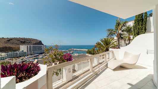 Utsikt fra en solterrasse over havet og en havn. (AI-generert tekst)