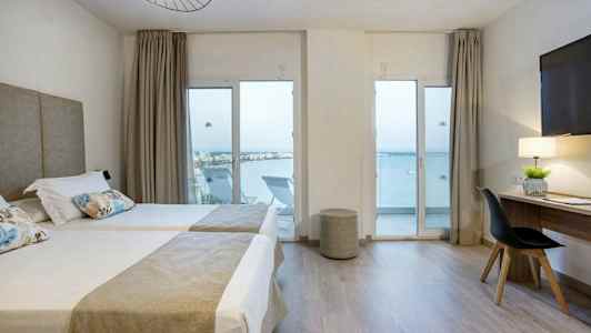 Hotellrom med to enkeltsenger, skrivebord og havutsikt gjennom glassdører. (AI-generert tekst)