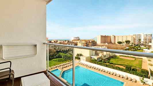 Balkong med utsikt over et svømmebasseng og omliggende bygninger. Solstoler står ved bassenget. (AI-generert tekst)