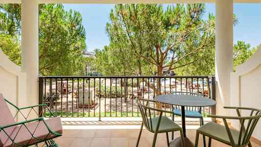 En balkong med bord, stoler og utsikt over frodige trær. (AI-generert tekst)