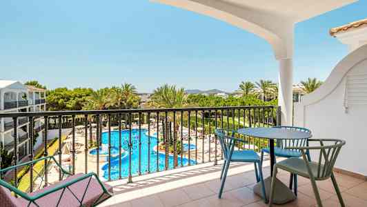 Utsikt fra en balkong med bord og stoler mot et basseng og omkringliggende grøntområde. (AI-generert tekst)