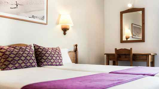 Et hotellrom med to enkeltsenger med lilla sengetøy, et speil og et skrivebord. (AI-generert tekst)