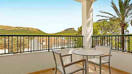 Balkong med bord og stoler, utsikt over landskap med åser og grøntområder. (AI-generert tekst)