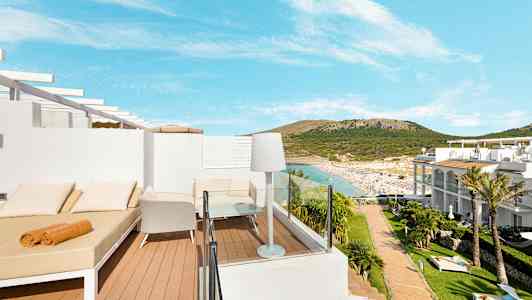 Utsikt over en terrasse med solsenger og stoler, med sandstrand og omkringliggende åser i bakgrunnen. (AI-generert tekst)