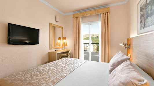 Et hotellrom med dobbeltseng, TV, skrivebord, speil og en balkong med utsikt. (AI-generert tekst)