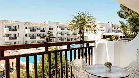 Utsikt fra balkong med bord og stoler mot hvit bygning og bassengområde. (AI-generert tekst)