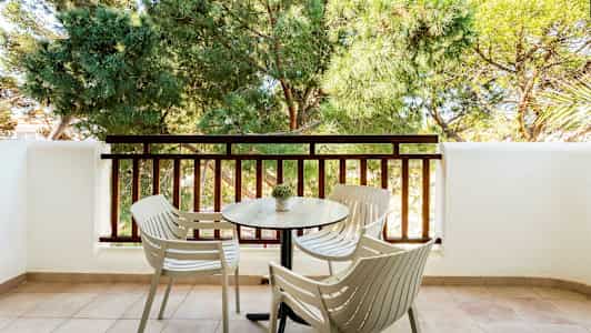 En balkong med fire stoler og et bord foran et rekkverk og grønne trær. (AI-generert tekst)