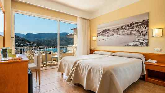 Et hotellrom med to enkeltsenger, et stort vindu med utsikt over en åsside og en balkong med stoler. (AI-generert tekst)