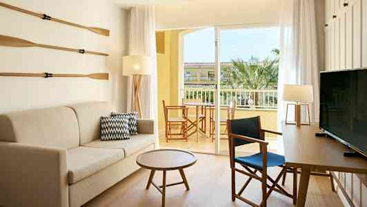 Et rom med sofa, bord og stoler. En dør fører til en balkong med utsikt. (AI-generert tekst)