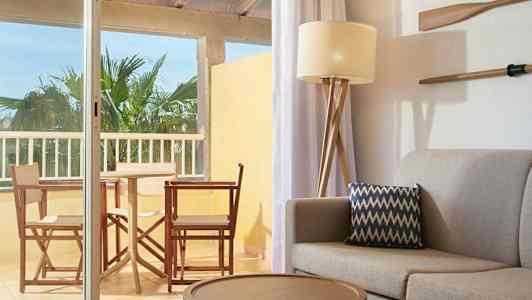 En innredning med sofa og pute i forgrunnen samt utsikt mot en møblert balkong. (AI-generert tekst)