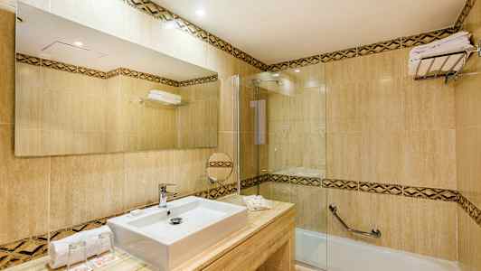 Et moderne baderom med fliser, en rektangulær vask, et stort speil og et badekar med glassvegg. (AI-generert tekst)