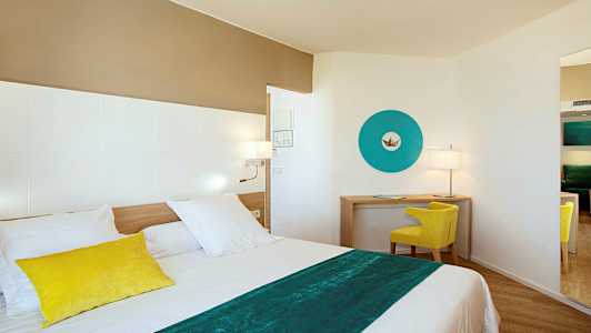 Et moderne hotellrom med en seng i forgrunnen, et skrivebordområde med en gul stol og en blå dekorativ veggdetalj. (AI-generert tekst)