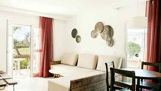 Et stue med lyse møbler, et stort vindu med røde gardiner og dekorasjoner på veggen. (AI-generert tekst)