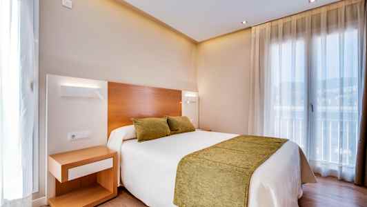 Et hotellrom med en dobbeltseng med grønne puter og sengeteppe. Et nattbord står ved siden av sengen. (AI-generert tekst)