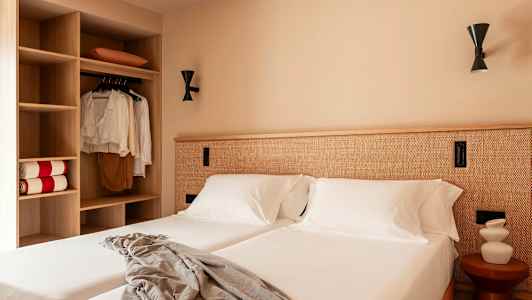 Et hotellrom med to senger, hvitt sengetøy og en garderobe til venstre. (AI-generert tekst)