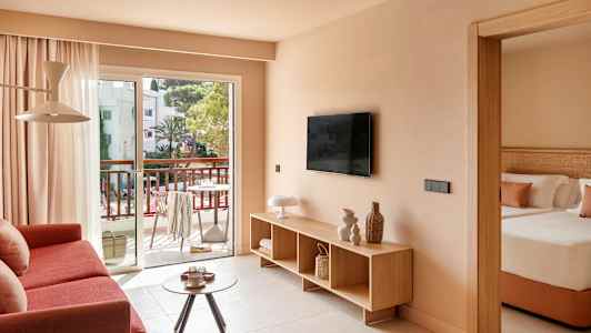 Stue med sofa, TV og utgang til balkong, samt ett delvis synlig soverom. (AI-generert tekst)