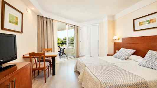 Bilde av et hotellrom med to enkeltsenger, et skrivebord med stoler og en balkong. (AI-generert tekst)