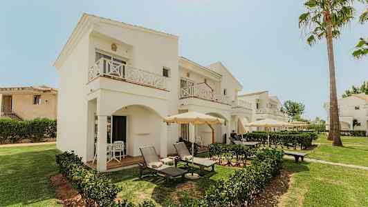 Hotellets hvite toetasjes bygninger med balkonger og uteplasser omgitt av grøntområder. (AI-generert tekst)