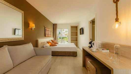 Et hotellrom med en sofa, en seng, et skrivebord med kaffemaskin og glass, samt en dør til en balkong. (AI-generert tekst)