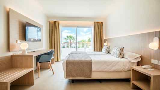 Moderne innredet hotellrom med seng, skrivebord og store glassdører mot en balkong. (AI-generert tekst)